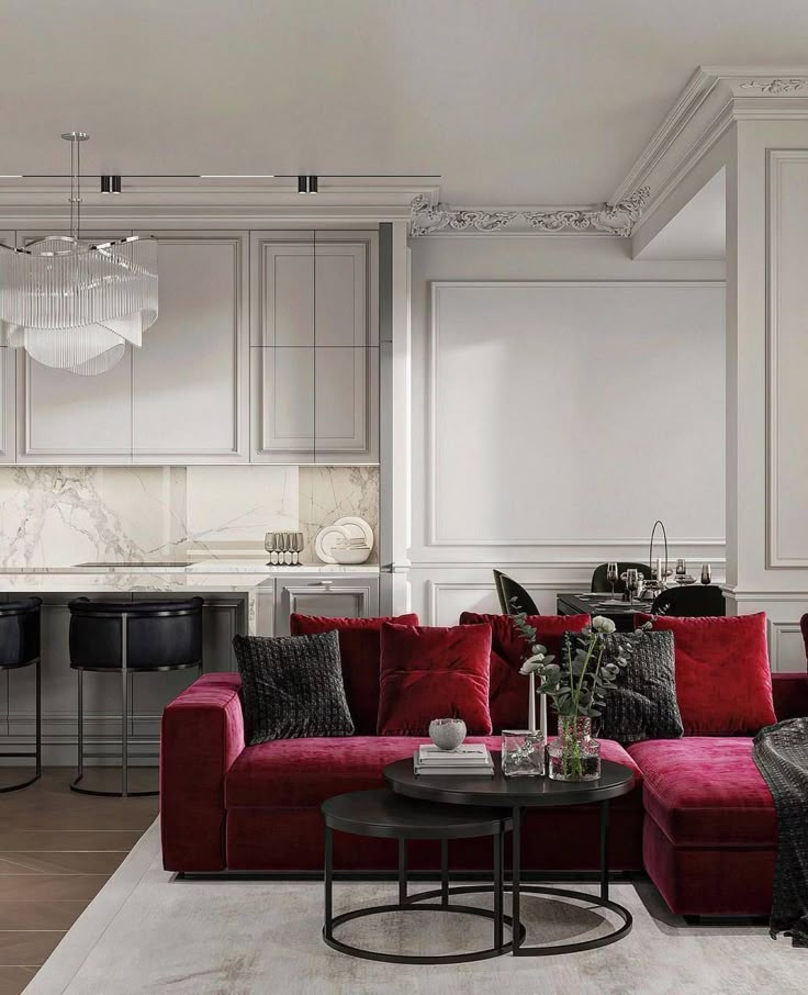 Luxurious living room with red velvet sofa, black chairs, marble accents, and elegant decor with a modern chandelier.