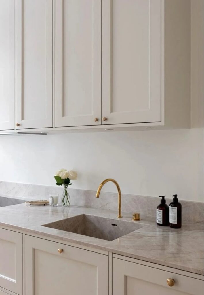 Modern kitchen with marble countertop, gold faucet, white cabinets, and decorative roses. Minimalist design elegance.