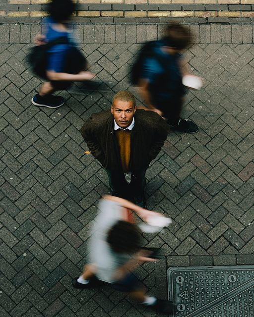 Man standing on a busy street, looking up, as people walk past him in motion blur, highlighting solitude in a crowd.