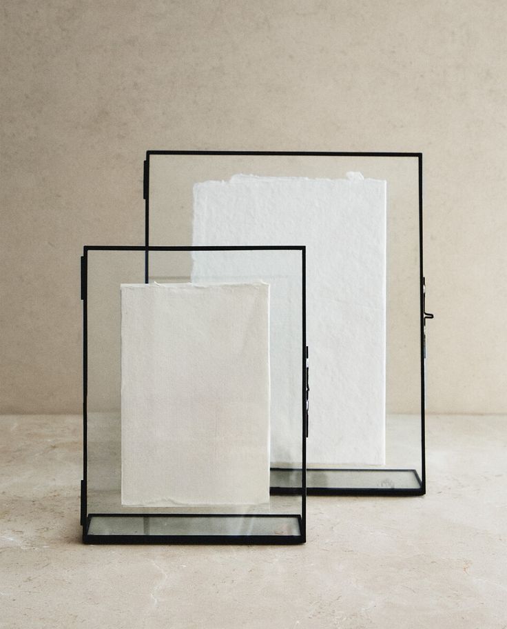 Minimalist display with handmade paper in black metal frames on a neutral background.