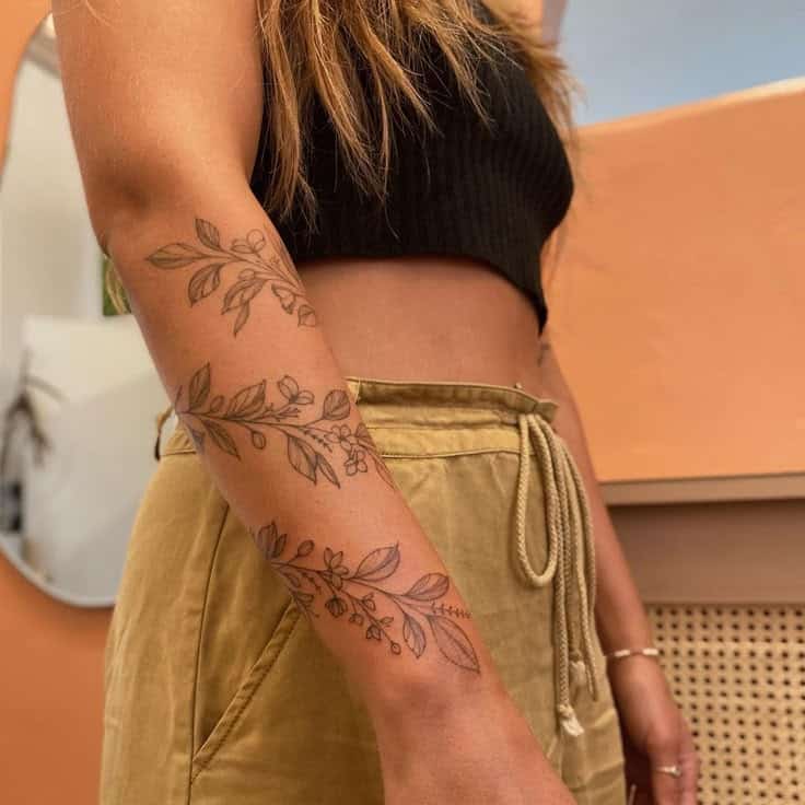 Woman with floral arm tattoo wearing black crop top and khaki pants.