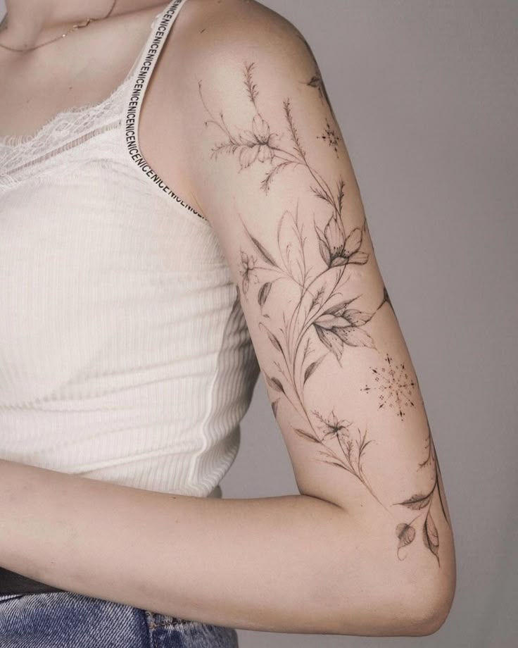 Arm with intricate floral tattoo in black ink, featuring delicate leaves and blossoms on a light background.