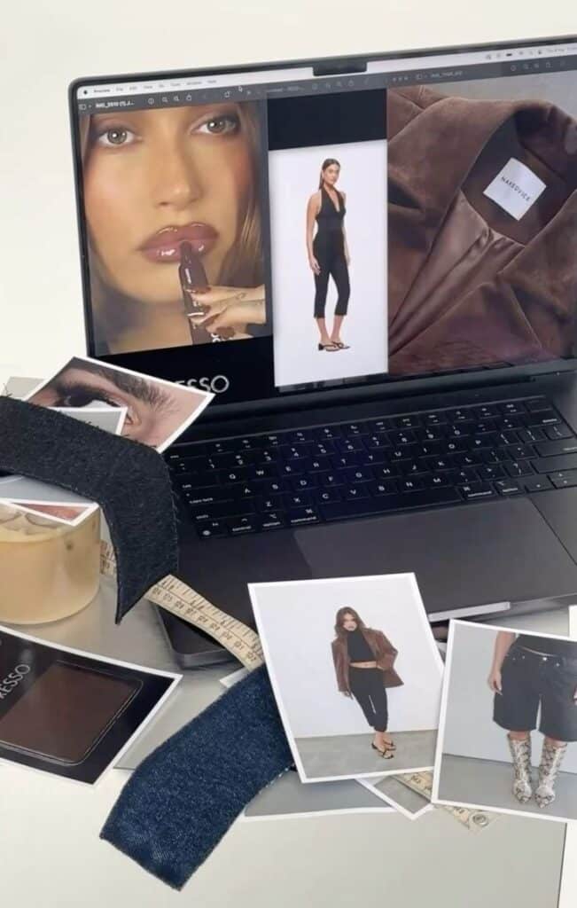 Laptop displaying fashion images, surrounded by fabric swatches and photos, suggesting fashion design planning.
