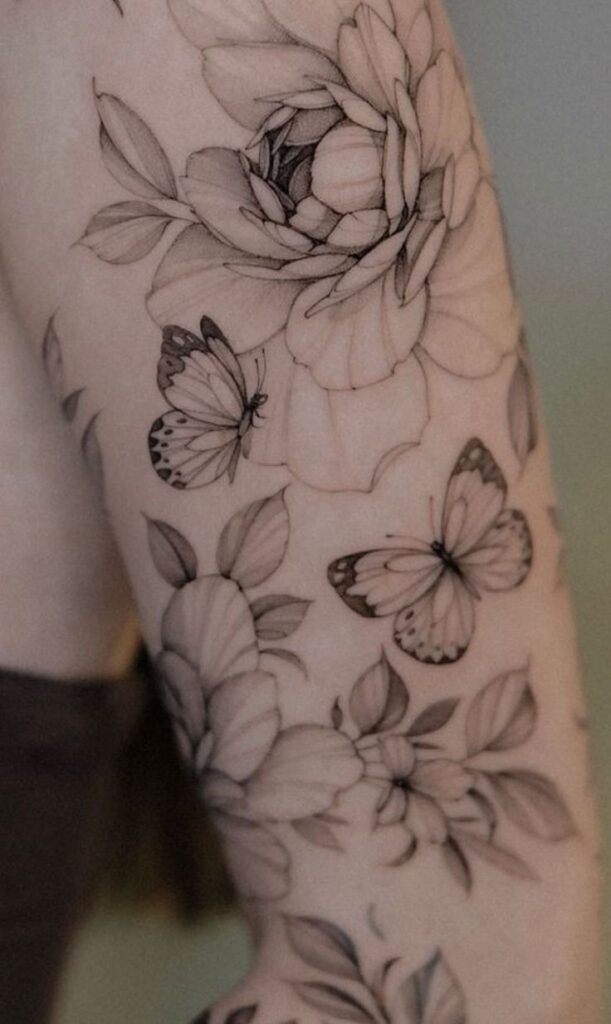 Black and grey floral tattoo on arm with butterflies, featuring detailed flowers and leaves.