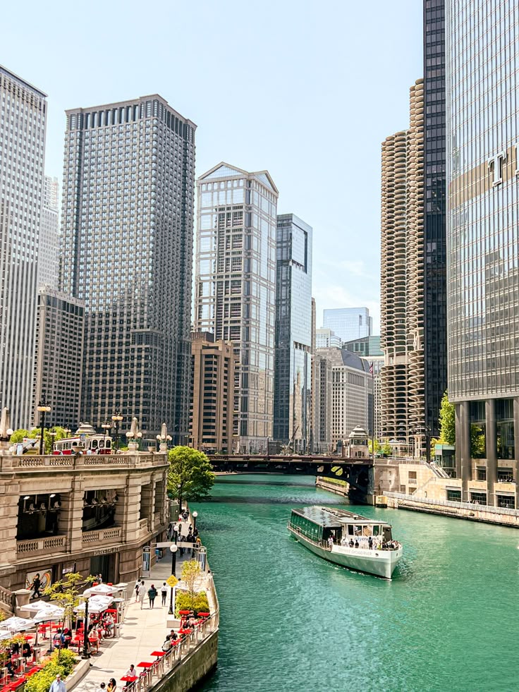 Chicago River with tour boat, surrounded by skyscrapers and riverside dining on a sunny day.