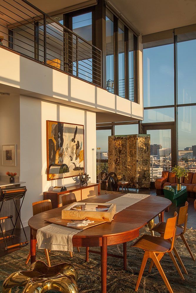 85b874e4-a8e8-4b8a-bd1d-e34c1d9a02a7 Modern loft interior with tall windows, elegant wooden dining table, and art pieces in warm natural light. | Sky Rye Design Modern loft interior with tall windows, elegant wooden dining table, and art pieces in warm natural light.