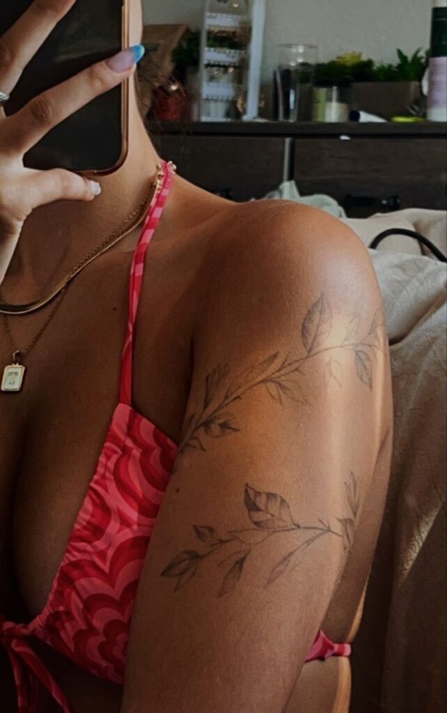 Woman with floral arm tattoo, wearing red bikini top, holding phone.