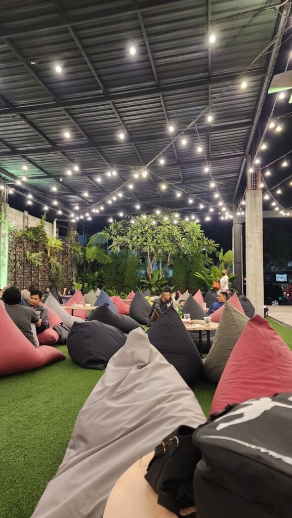 Outdoor seating area with string lights, cozy bean bags, and lush greenery, creating a relaxed ambiance for social gatherings.