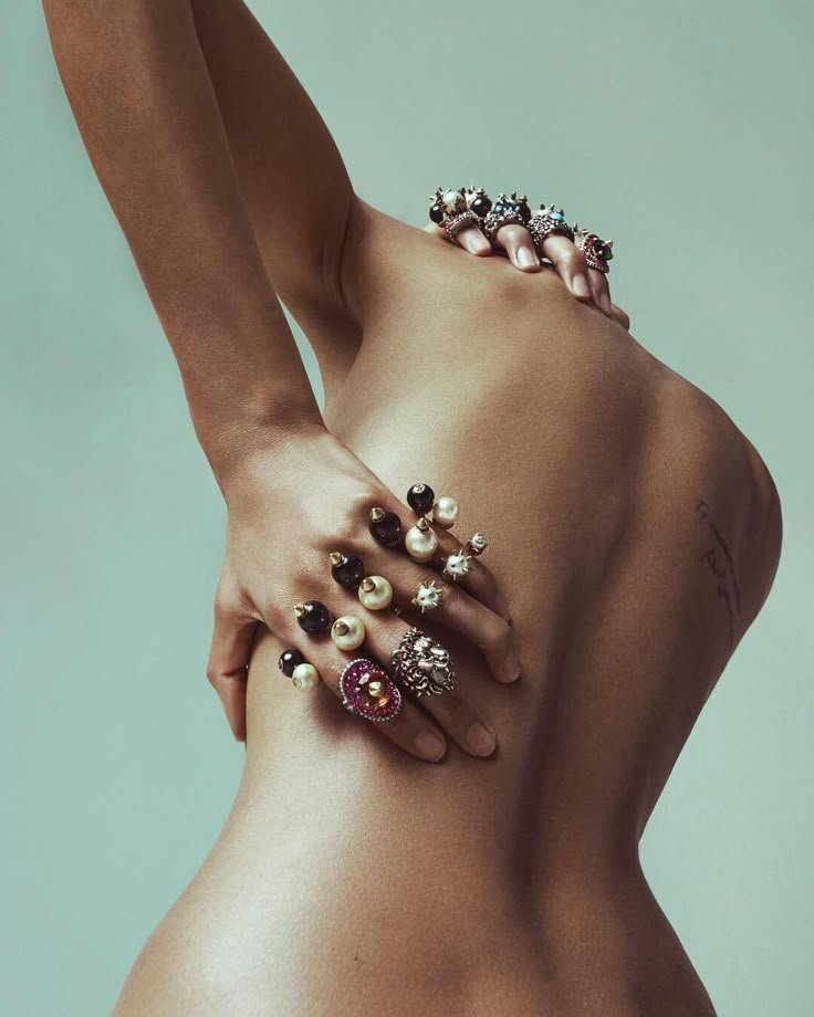 Person showcasing eclectic rings on both hands against a bare back. Fashion jewelry focus on pearls and intricate designs.