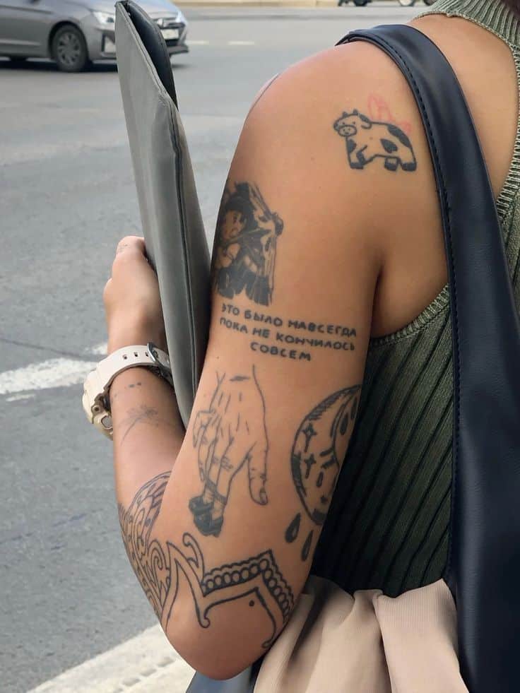 Person with various tattoos on arm, standing on a street corner holding a folder, wearing a green top.