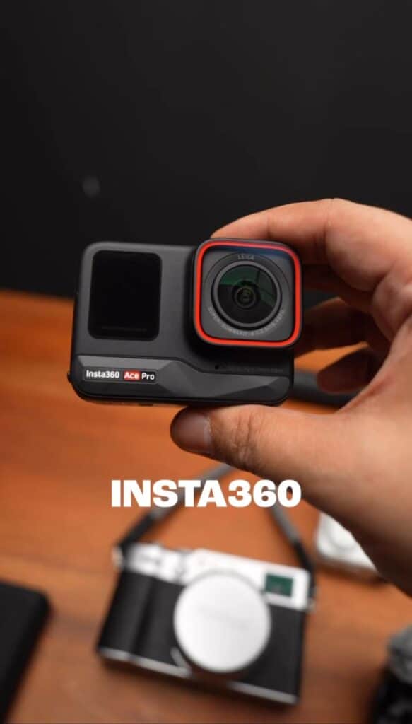 Hand holding Insta360 Ace Pro camera, with lens and display visible, wooden surface background.