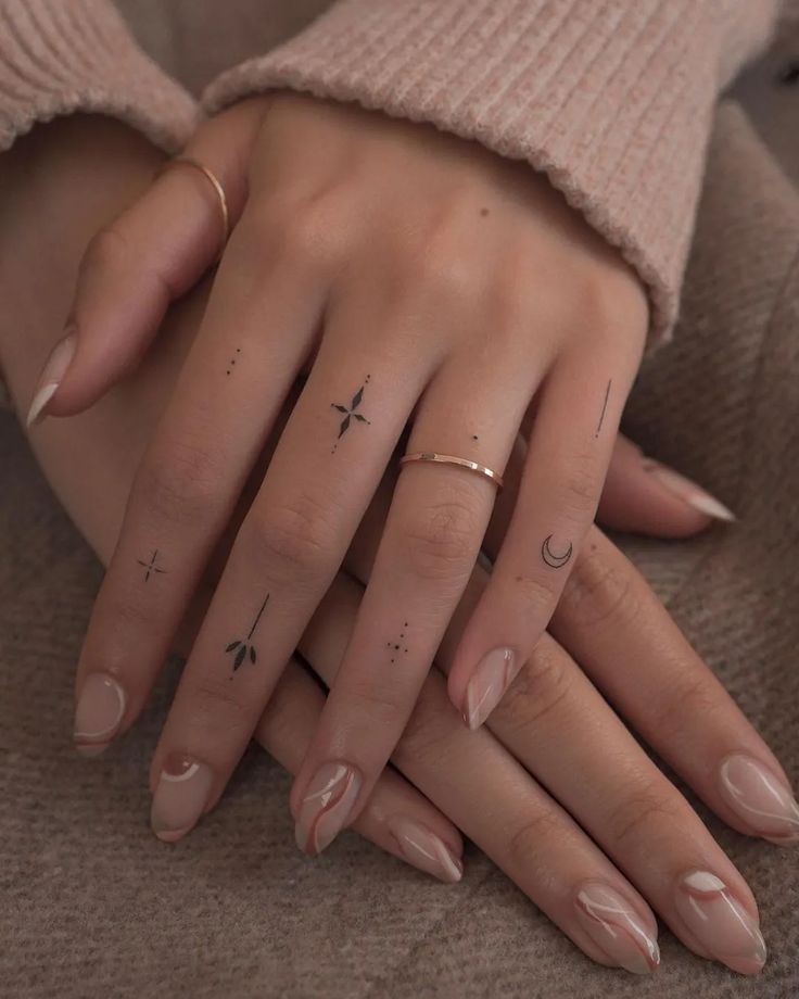 Close-up of hands with minimal tattoos and elegant nail art, showcasing delicate rings on fingers.