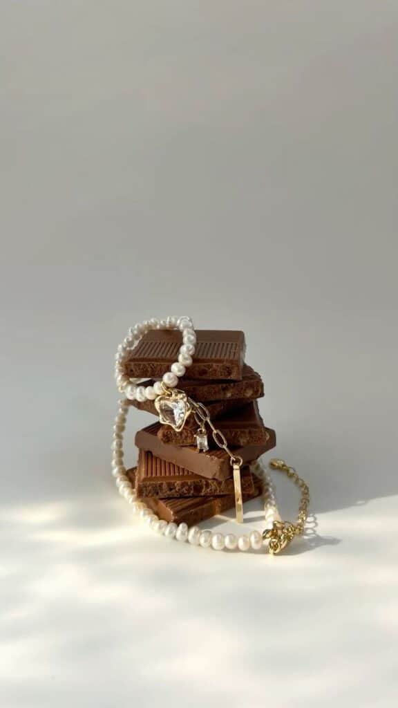 Pearl necklace draped over stacked chocolate bars, elegant minimal aesthetic.