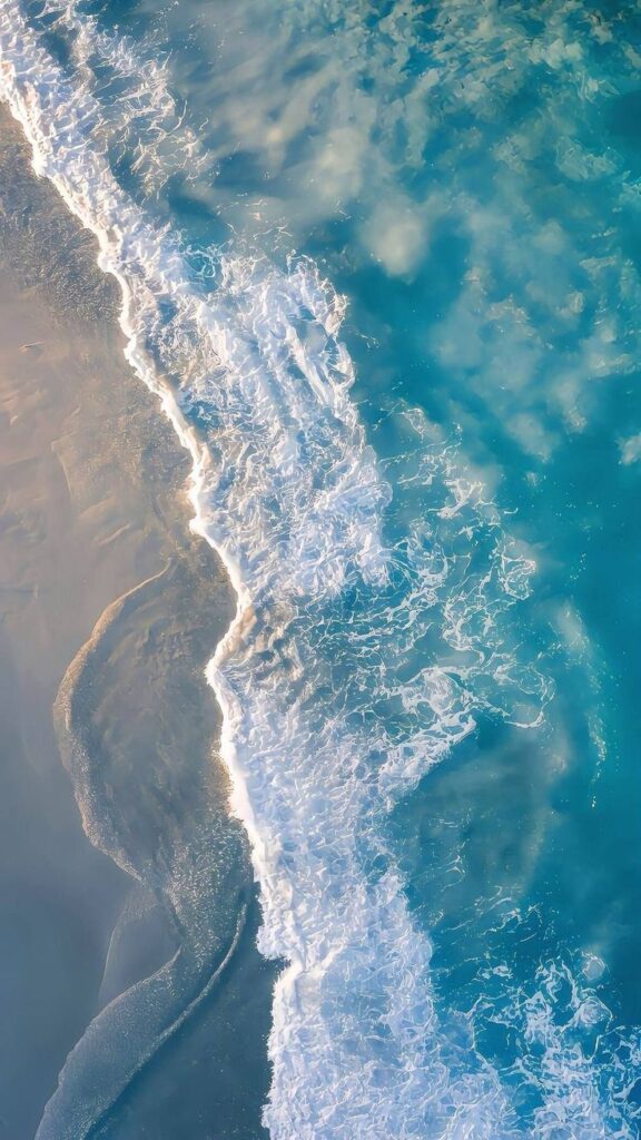 Aerial view of turquoise ocean waves gently lapping onto a sandy beach, creating a serene coastal scene.