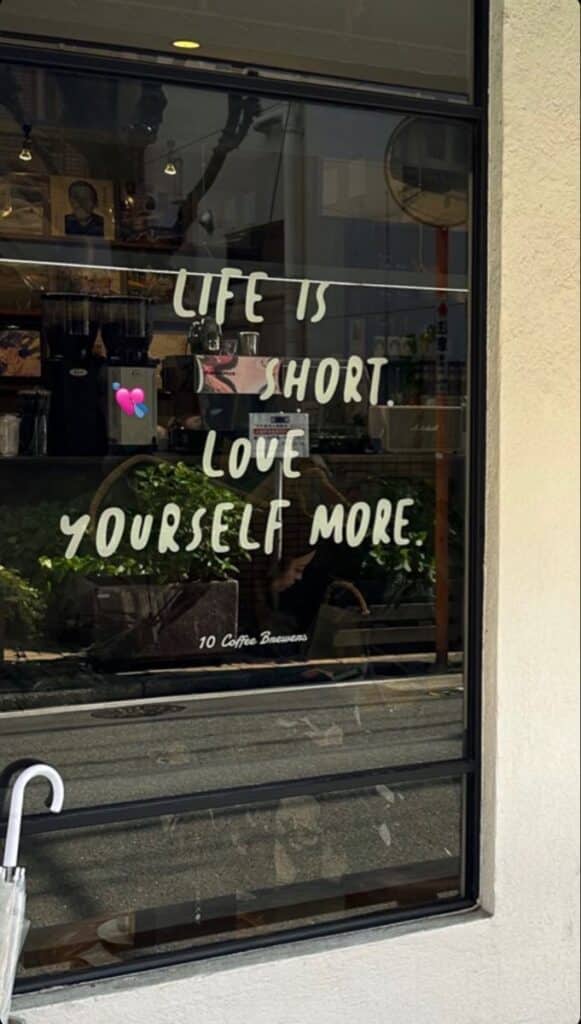 Cafe window with motivational text: Life is short, love yourself more at 10 Coffee Brewers.