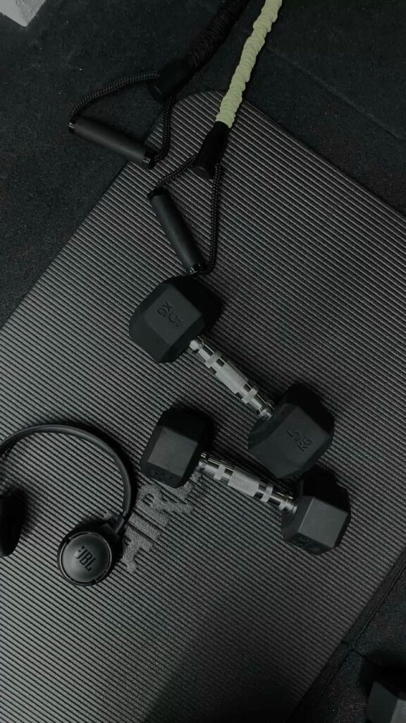 Dumbbells, resistance bands, and headphones on a gym mat, essential fitness equipment for a home workout.