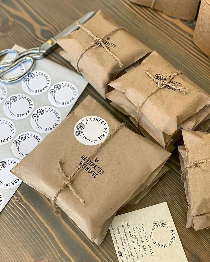 Handcrafted gift packages tied with twine, labeled Ashley Marie, on wooden surface with scissors and stickers nearby.
