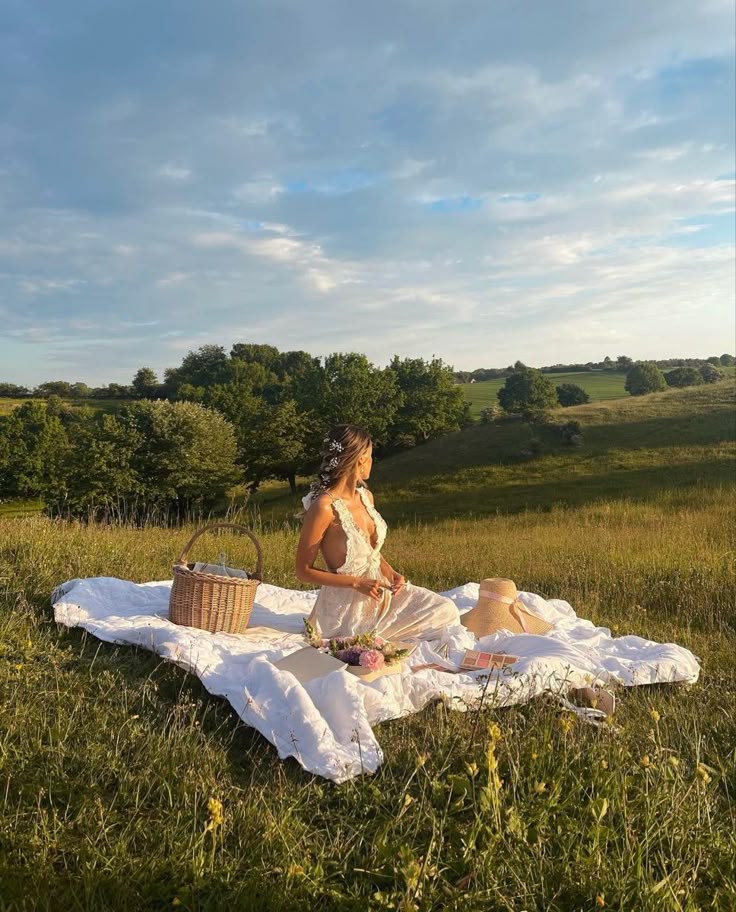 Woman enjoying a picnic on a grassy field with a basket and book under a clear sky.