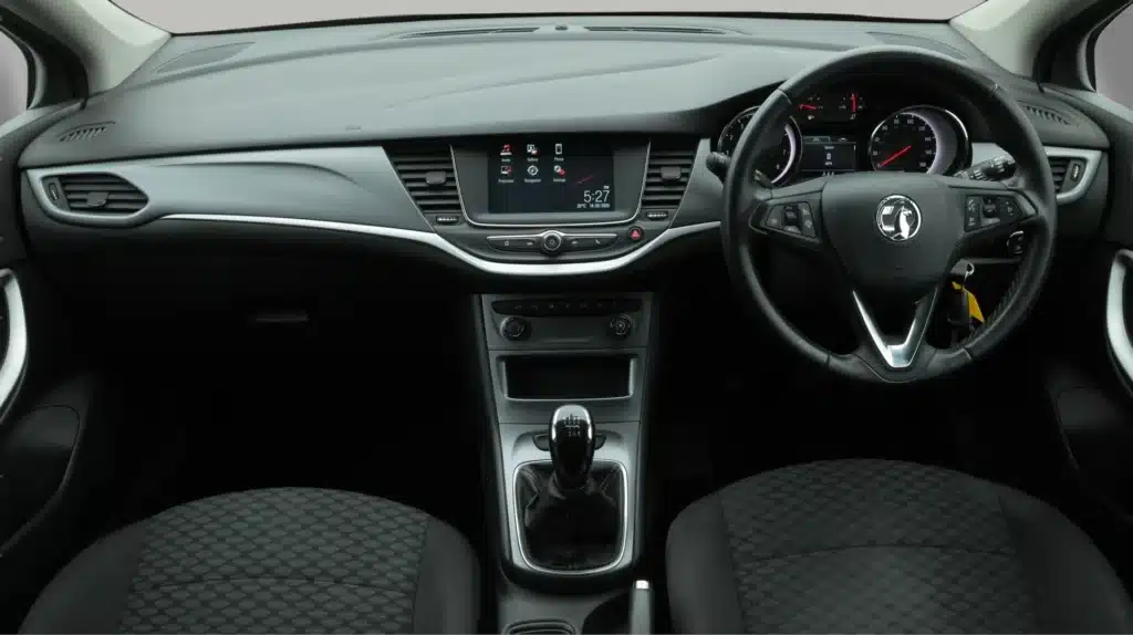 Modern car dashboard with touch screen, manual gear shift, and steering wheel controls.