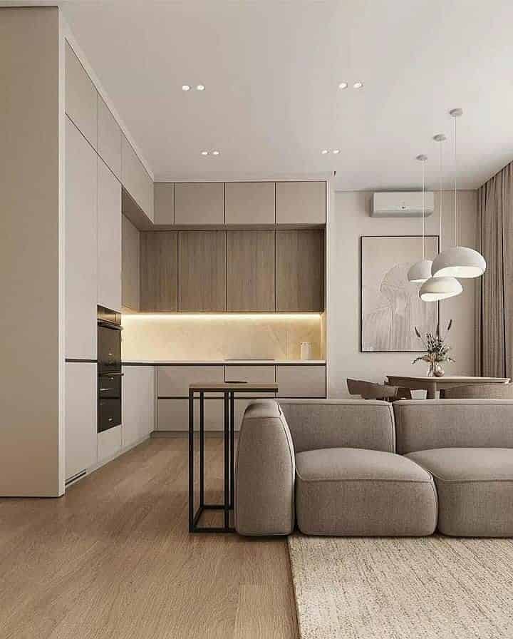 Modern minimalist living area with open kitchen, sleek cabinetry, beige sofa and pendant lights.