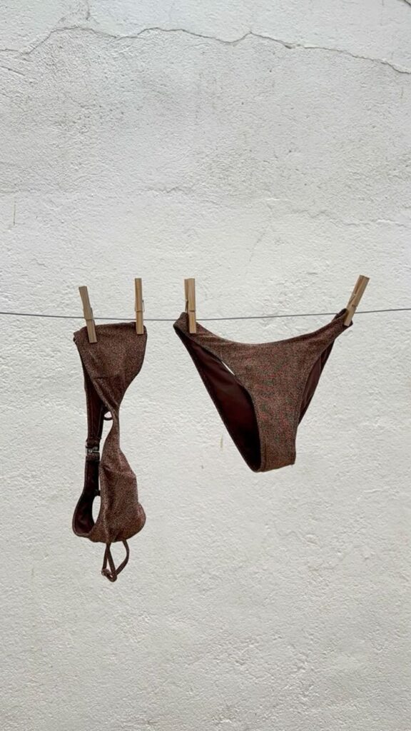 Brown bikini hanging on a clothesline against a textured white wall background.