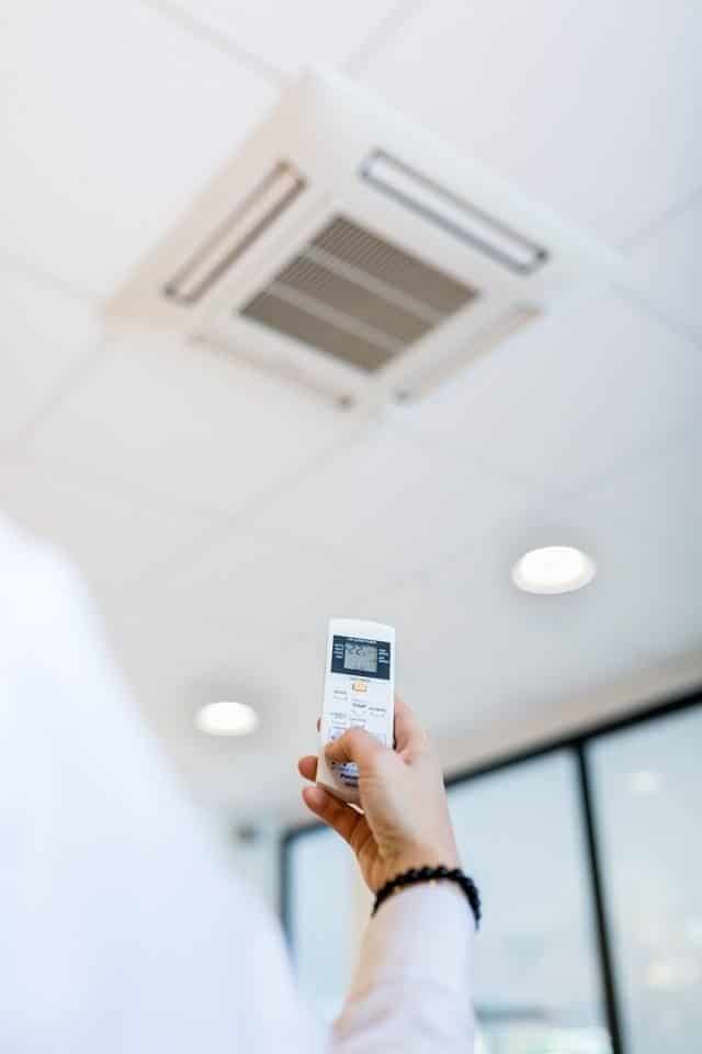 Person adjusting ceiling air conditioner with a remote control in a modern office setting.