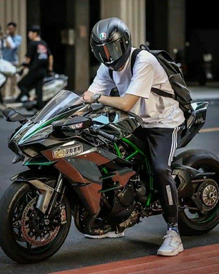 A person in a helmet sits on a sleek, modern motorcycle on an urban street, wearing sporty attire and a backpack.