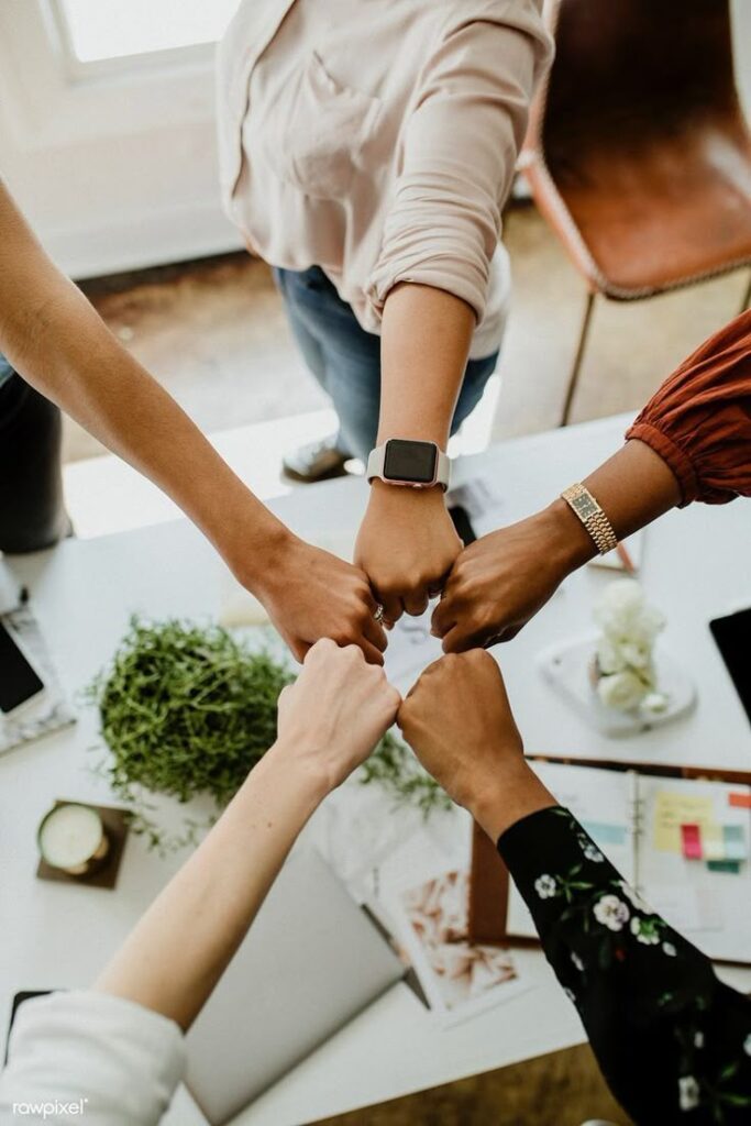 Team collaboration: five diverse hands joining for a fist bump over a desk to symbolize teamwork and unity.