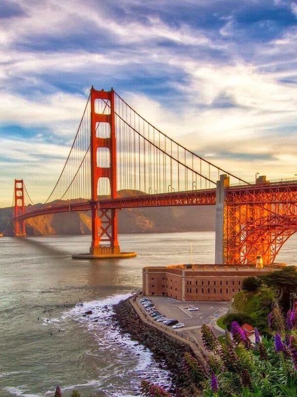 Golden Gate Bridge at sunset with vibrant flowers in the foreground and a scenic ocean view, San Francisco.