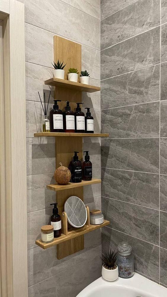 Wooden bathroom shelves with toiletries, plants, and a mirror on gray tiled wall for stylish storage.