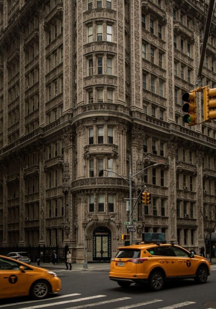 Ornate historic building on city street corner with yellow taxis in motion near traffic lights.