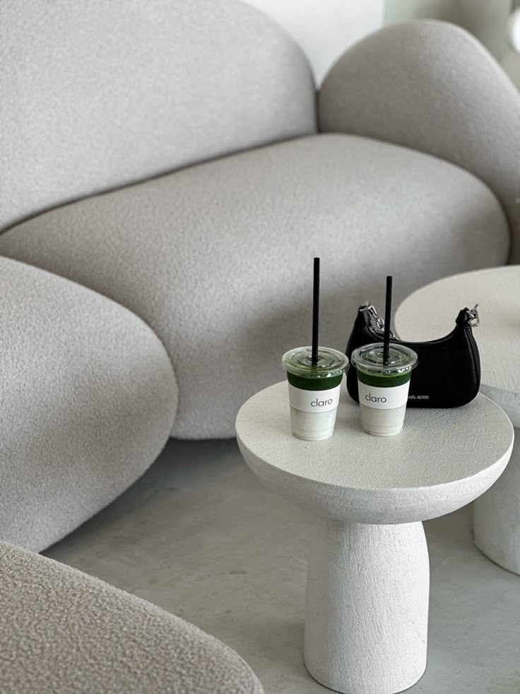 Minimalist lounge setting with two matcha drinks on a small white table, beside a black purse.