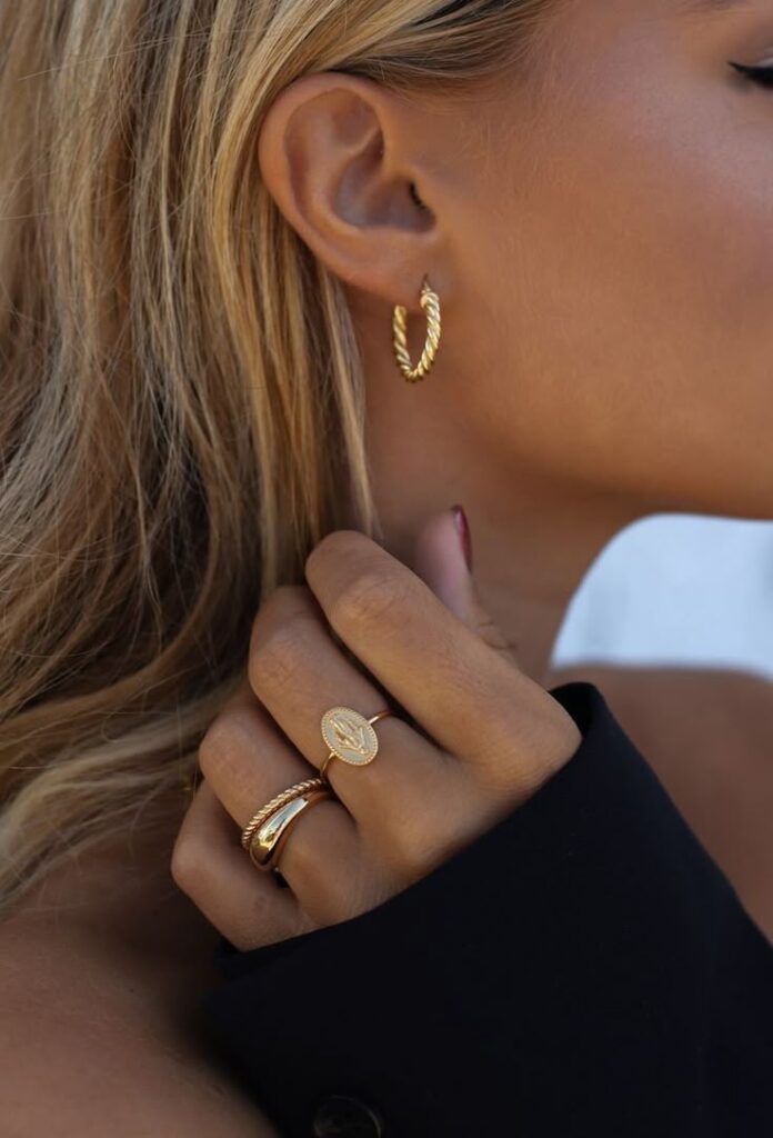 96178518-5644-47c3-aa84-166bff652237 Woman wearing gold hoop earrings and rings showcases elegant jewelry style. | Sky Rye Design Woman wearing gold hoop earrings and rings showcases elegant jewelry style.