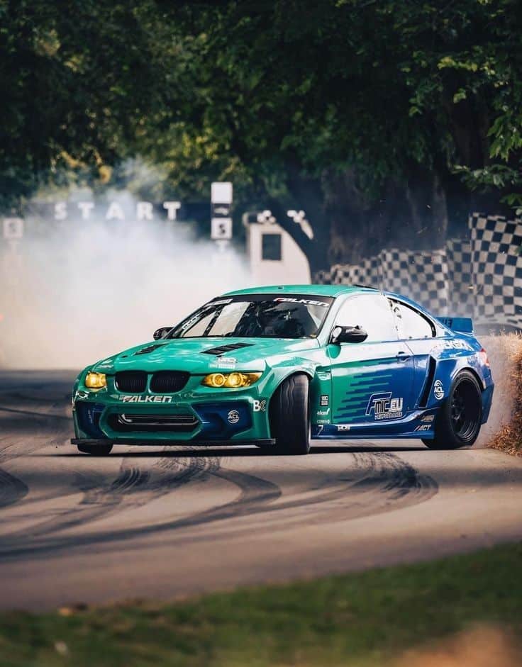 Green and blue drift car powersliding on a track, leaving tire marks and smoke behind at a motorsport event.