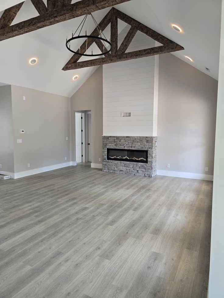 Modern living room with vaulted ceiling, exposed beams, stone fireplace, and wood flooring.