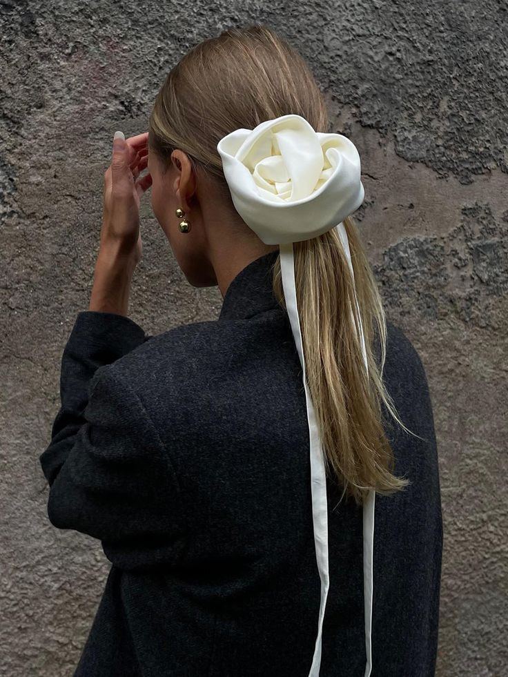 Woman with elegant satin hair accessory and gold earrings, styled in a neat ponytail against a textured wall.