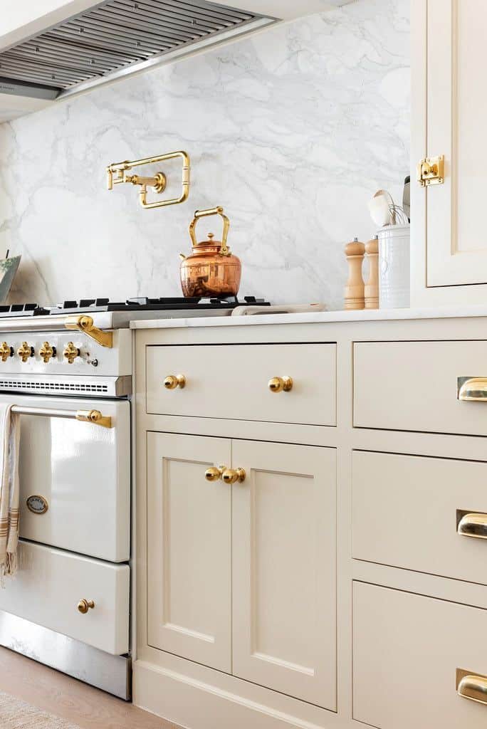 Add charm and character to your cabinetry with the Elegant kitchen with marble backsplash, vintage stove, copper kettle, and cream cabinets with gold hardware. | Sky Rye Design Elegant kitchen with marble backsplash, vintage stove, copper kettle, and cream cabinets with gold hardware.