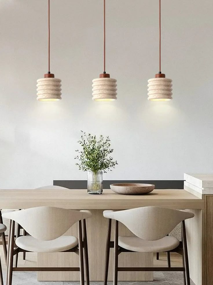 Modern dining area with three hanging pendant lights, wooden table, chairs, and a vase with greenery for minimalist decor.