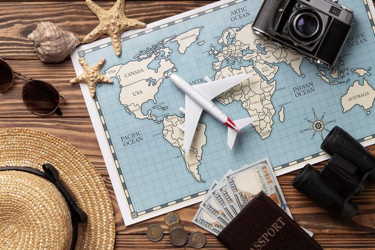 Travel essentials on world map: toy plane, camera, passport, money, hat, sunglasses, and binoculars on wooden background.