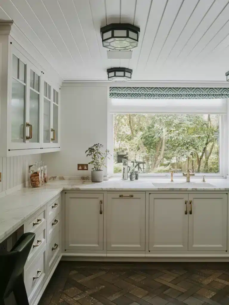 Stylish white kitchen with marble countertops, large window, and garden view, perfect for a cozy and elegant cooking space.