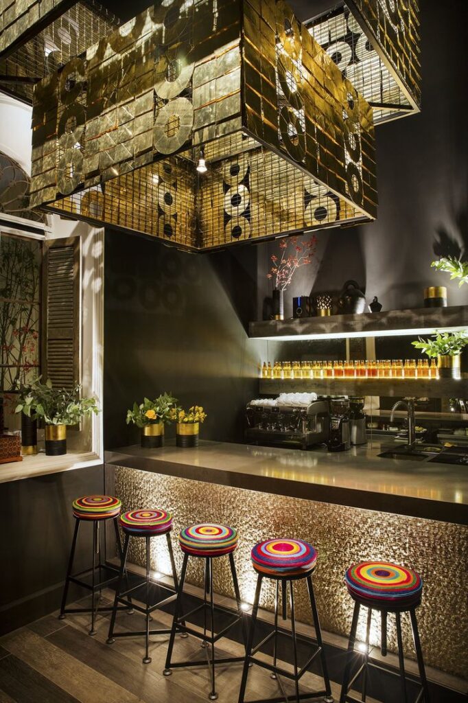 Stylish cafe interior with colorful bar stools, gold accents, and warm lighting creating an inviting atmosphere.