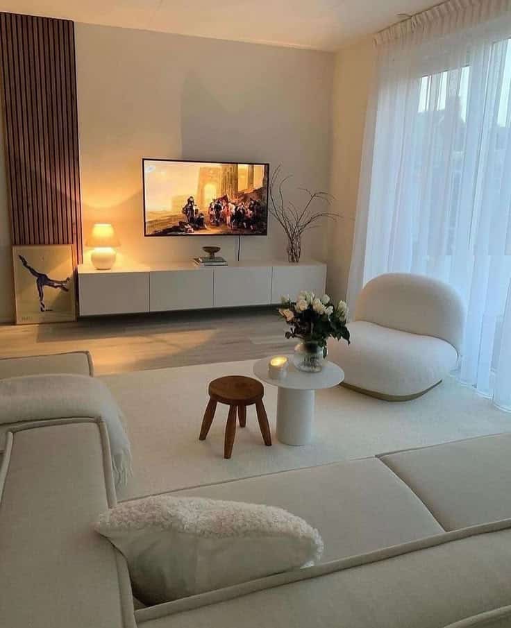 Modern living room with cozy seating, a TV, and warm lighting, featuring minimalist decor with wooden and white accents.
