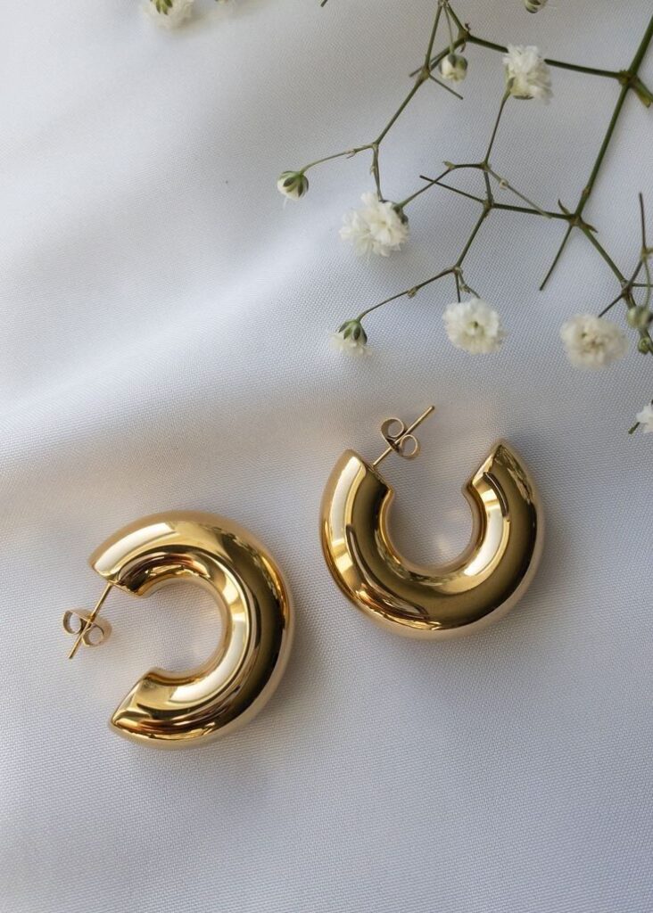 Gold crescent earrings on white fabric with delicate baby's breath flowers. Elegant jewelry display.