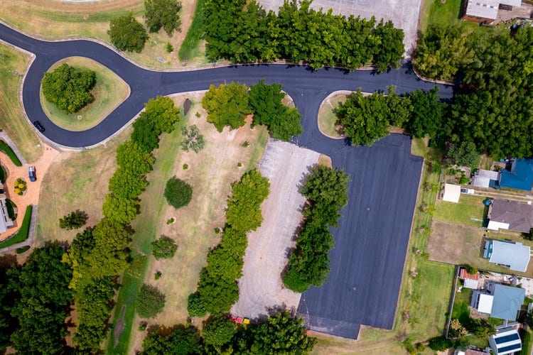 Aerial view of a parking lot and road surrounded by lush green trees and residential area.