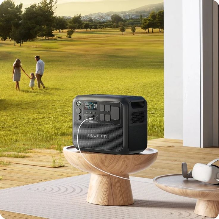 Portable power station on a table outdoors, with a family walking on a grassy field in the background.