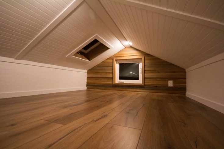 Cozy attic space with wooden floors and slanted ceiling, featuring a small window for natural light.