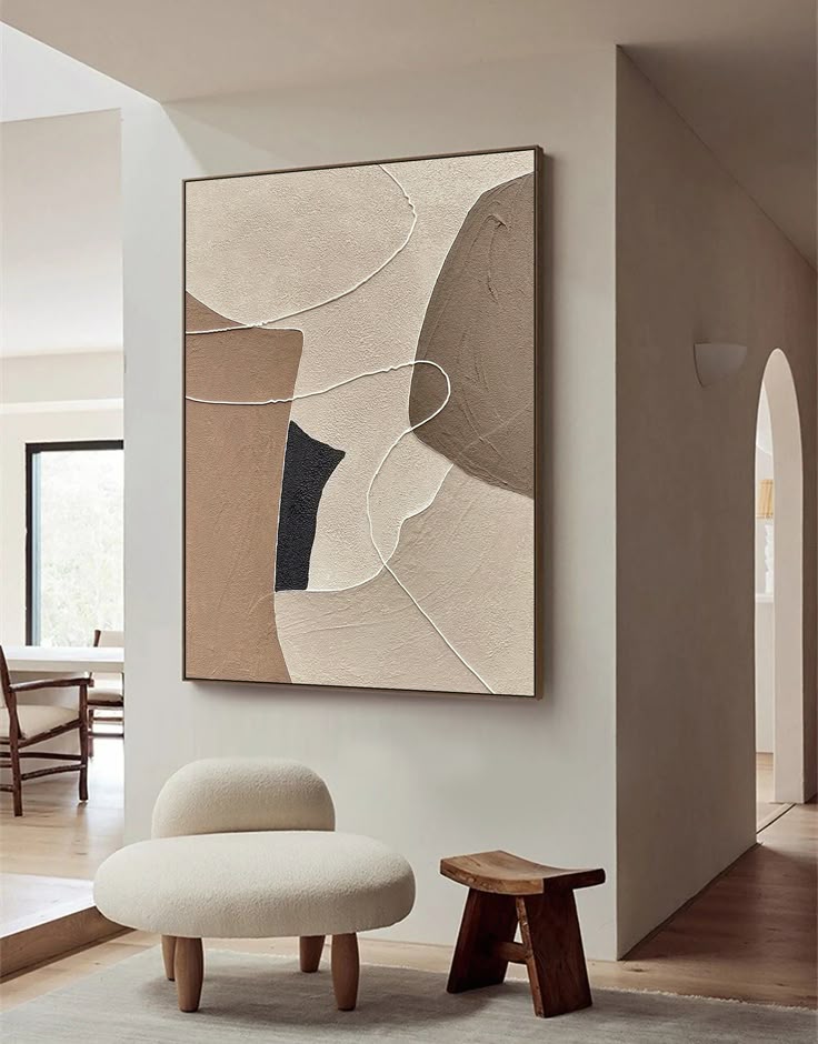 Abstract painting on wall in modern living room with beige chair and wooden stool, featuring neutral tones and minimalist design.