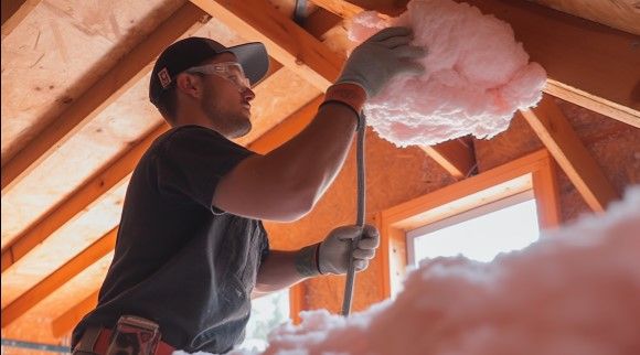 Worker installing attic insulation in a wooden house, enhancing energy efficiency and home warmth.