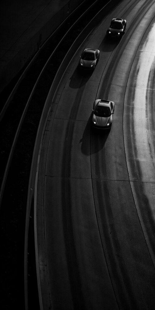 Aerial view of cars driving on a curving highway at night, showcasing dramatic lighting and motion.