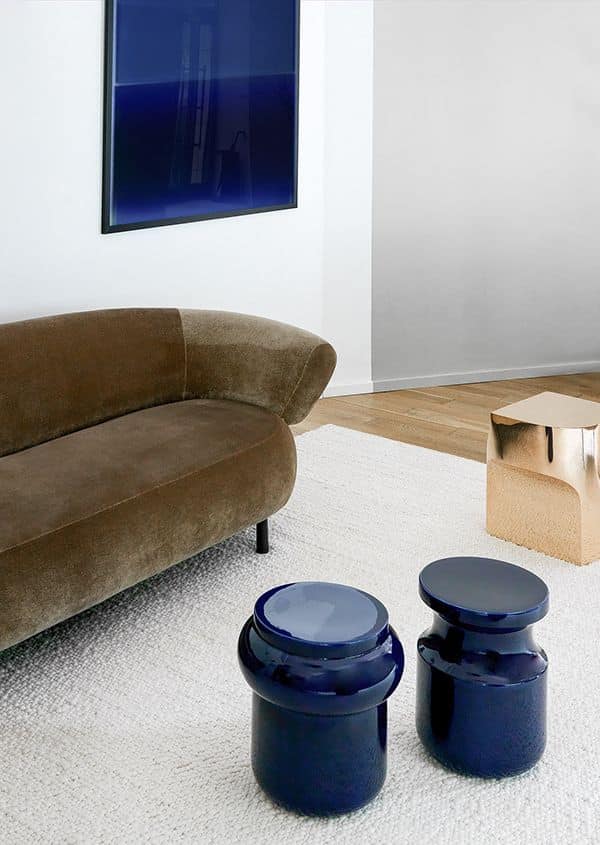 Modern living room with a brown sofa, blue side tables, and abstract art on a white wall.